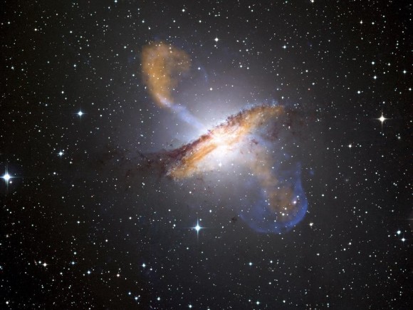 Los chorros que se aprecian en la imagen son electrones expulsados del centro de la galaxia. En azul, las emisiones de rayos X, en naranja la banda milimétrica, y en imagen óptica, las estrellas que se ven en la imagen. Imagen: Rayos X - NASA/CXC/CfA/R.Kraft et al. Submilímetro - MPIfR/ESO/APEX/A.Weiss et al. Visible - ESO/WFI.