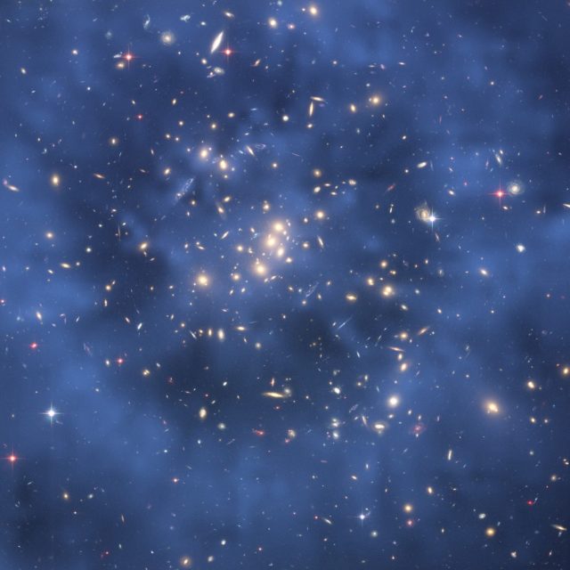 El efecto de onda gravitacional permite deducir la distribución de un anillo de materia oscura en esta imagen de un cúmulo de galaxias, a la que se ha incorporado como un halo de color azul. Wikimedia Commons